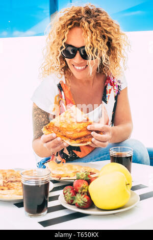 De beaux longs cheveux blonds bouclés cheerful woman eating pizza italienne en plein air restaurant ou terrasse - Accueil de jeunes femmes à la mode avec tatoo et occasionnels Banque D'Images