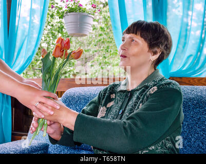 Femme âgée accepte un bouquet de tulipes rouges le jour de la mère maison de vacances Banque D'Images