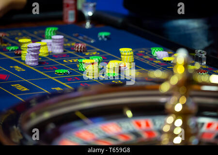 Table de roulette avec des mains de poser des jetons dans un casino. La roue de roulette à l'avant-plan. Jouer jeu. Les gens méconnaissables. Banque D'Images