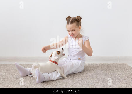 Les enfants, les animaux et les chiens concept - enfant fille en pyjama assis sur le plancher et jouer avec puppy Banque D'Images