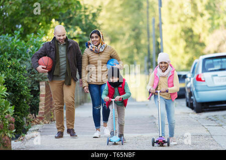 Regarder la famille musulmane et riding scooter on sidewalk Banque D'Images