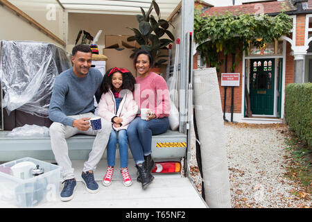 Happy Family portrait de boire du thé à l'arrière du camion de déménagement à l'extérieur de maison neuve Banque D'Images