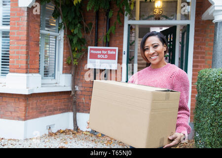 Portrait smiling woman, déménagement dans la nouvelle maison, holding cardboard box outside house Banque D'Images