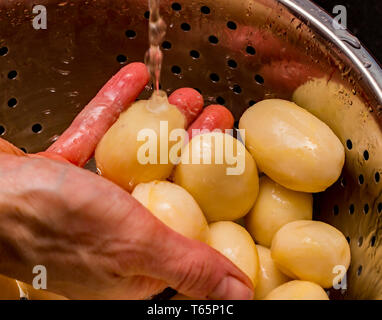 Close up de cuire les pommes de terre pelées de rinçage (Solanum tuberosum) sous le robinet dans une passoire en acier inoxydable. Banque D'Images