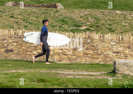 Un surfer carrying his surfboard et marcher le long du sentier du littoral sur la Pointe à Newquay en Cornouailles. Banque D'Images