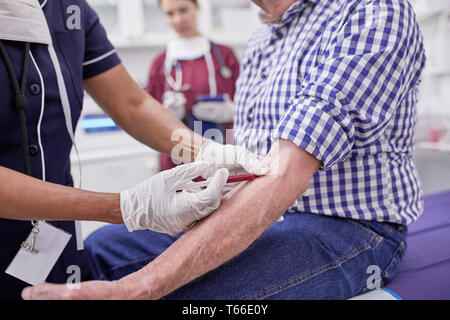 Femme médecin une prise de sang senior male patient en salle d'examen clinique Banque D'Images