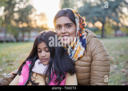 Portrait smiling mother en hijab sitting in autumn park avec fille Banque D'Images