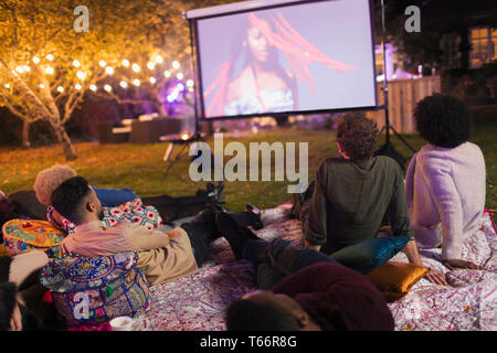 Les amis regarder la vidéo sur l'écran de projection in backyard Banque D'Images