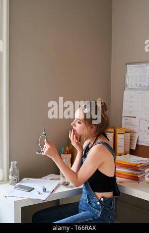 Young woman applying lip gloss dans mirror Banque D'Images