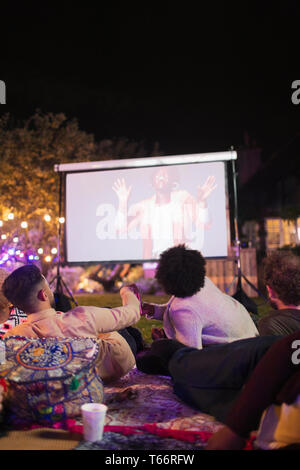 Les amis regarder la vidéo sur l'écran de projection in backyard Banque D'Images