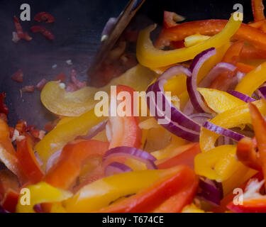 Une casserole d'oignons rouges (Allium cepa), poivrons rouges (capsicum) et les poivrons jaunes la cuisson dans une poêle anti-adhésive sur la plaque de cuisson. Banque D'Images
