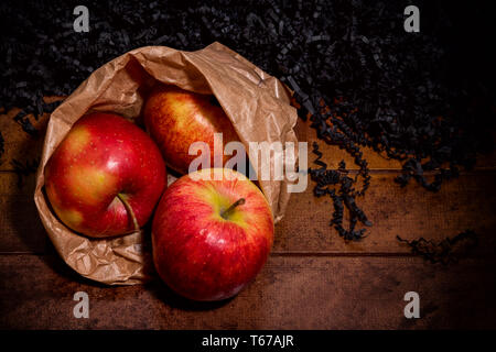 3 pommes fraîchement cueillies dans un sac en papier couché sur une surface en bois brun Banque D'Images