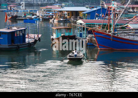 Une personne rame un petit bateau à travers un port rempli de bateaux colorés et de maisons flottantes. Banque D'Images