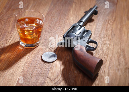 Wild West revolver avec verre de whisky et de la glace avec de vieux silver dollar sur table bar en bois Banque D'Images