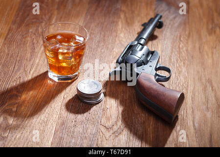 Wild West revolver avec verre de whisky et de la glace avec de vieux silver dollar sur table bar en bois Banque D'Images