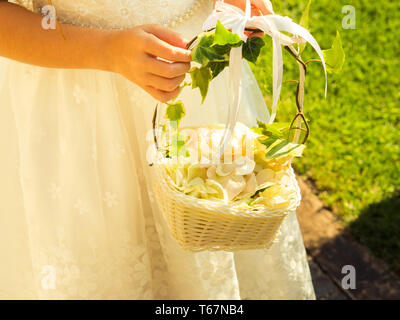 Flower Girl in white dress holding panier de pétales de rose dans le jardin de l'église Banque D'Images