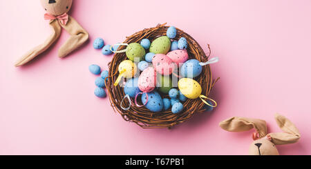 La décoration des œufs de Pâques colorés dans un nid et les lapins sur fond rose pastel. Mise à plat Banque D'Images