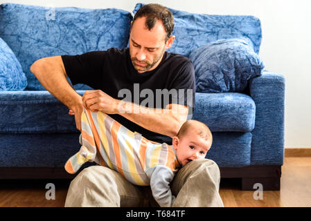 Père débutant changer les vêtements de son bébé avec effort dans le salon de sa maison. Banque D'Images