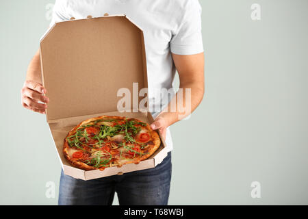 Young man holding box avec pizza savoureuse sur fond clair Banque D'Images