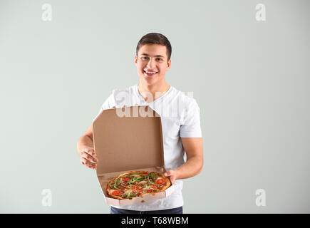 Young man holding box avec pizza savoureuse sur fond clair Banque D'Images