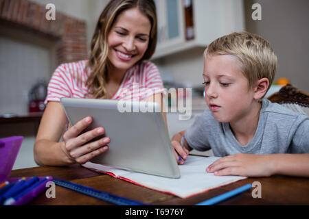 Mère à l'aide d'une tablette numérique tout en aidant les fils avec ses devoirs Banque D'Images