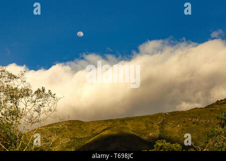 La presque pleine lune s'élève au-dessus un nuage dense dans les montagnes andines de Colombie, au coucher du soleil. Banque D'Images
