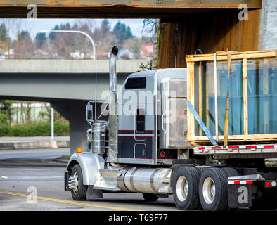 Big Rig classique gris et noir semi long haul truck transport windows de feuilles de verre dans des boîtes de bois fixé sur une semi-remorque sous lo Banque D'Images