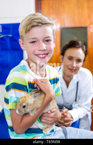 Portrait de jeune garçon tenant un lapin en face de femme vet Banque D'Images