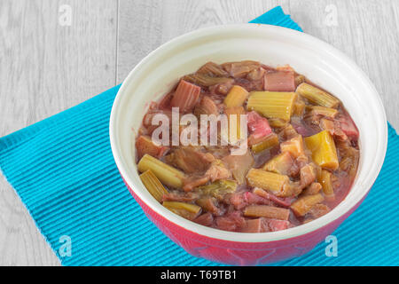 Compote de rhubarbe dans un bol sur un napperon bleu avec un fond en bois gris Banque D'Images