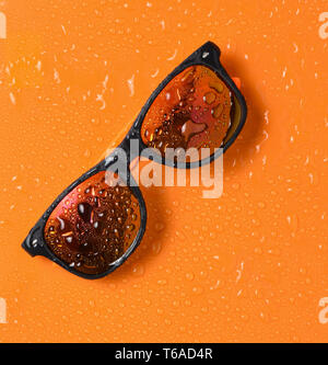 Fashion lunettes de soleil dans les gouttes d'eau sur un fond orange lumineux. Vue d'en haut. Banque D'Images