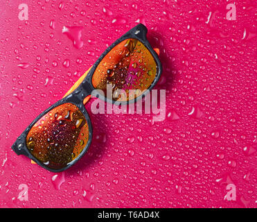 Fashion lunettes de soleil dans les gouttes d'eau sur un fond rose vif. Vue d'en haut. Banque D'Images