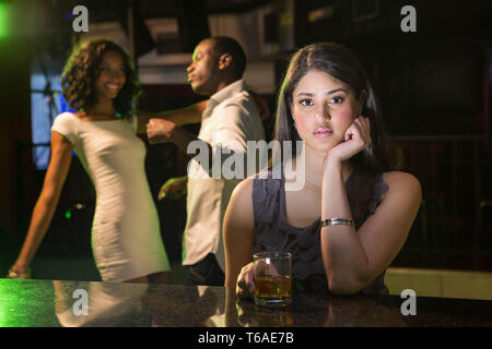 Malheureuse femme assise au comptoir du bar et couple dancing derrière elle Banque D'Images