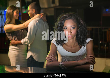 Malheureuse femme assise au comptoir du bar et couple dancing derrière elle Banque D'Images