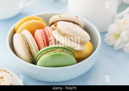 Macarons français colorés avec différents matériaux dans un bol pour le dessert. Fond bleu. Banque D'Images