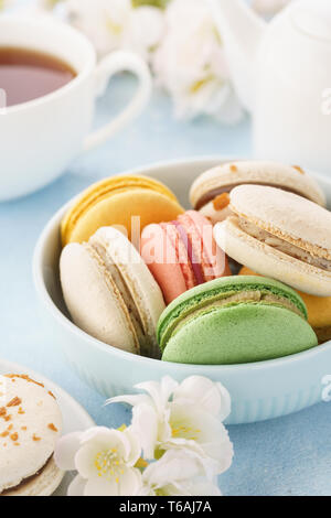 Macarons français colorés avec différents matériaux dans un bol pour le dessert. Fond bleu. Banque D'Images