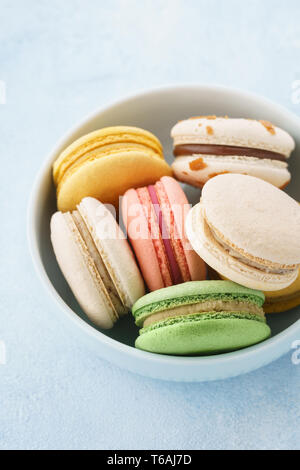 Macarons français colorés avec différents matériaux dans un bol sur fond bleu. Banque D'Images