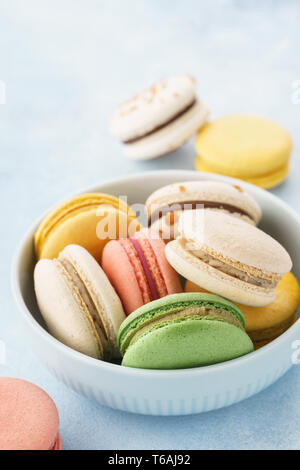 Macarons français colorés avec différents matériaux dans un bol sur fond bleu. Copier l'espace. Banque D'Images