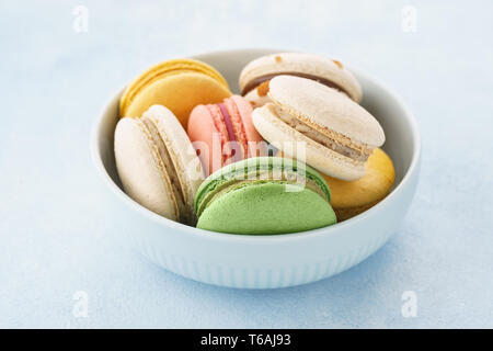 Macarons français colorés avec différents matériaux dans un bol sur fond bleu. Banque D'Images