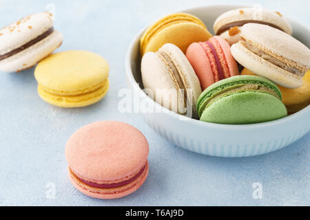 Macarons français colorés avec différents matériaux dans un bol sur fond bleu. Banque D'Images