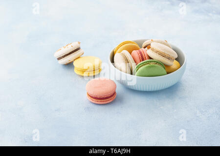 Macarons français colorés avec différents matériaux dans un bol sur fond bleu. Copier l'espace. Banque D'Images