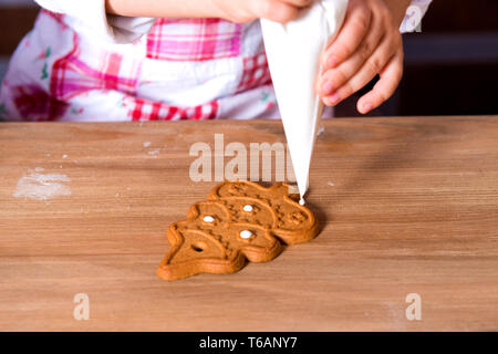 Un gros plan de l'épice de Noël sous la forme d'un Nouvel An des arbres se trouve sur la table. Fille orne les cookies avec glaçage sucré. Banque D'Images