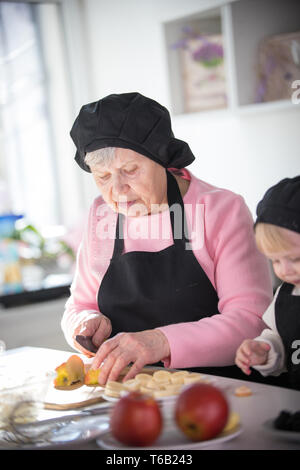 Une vieille femme une coupe sur des morceaux de pomme avec une petite fille dans la cuisine Banque D'Images