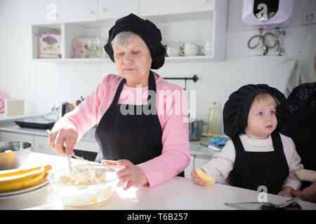 Une vieille femme faire des crêpes avec une petite fille dans la cuisine. Faire de la pâte dans le bol Banque D'Images