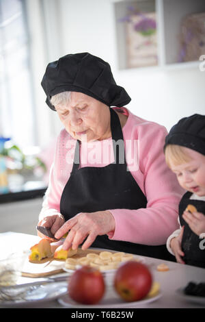 Une vieille femme une pomme de coupe avec une petite fille dans la cuisine Banque D'Images