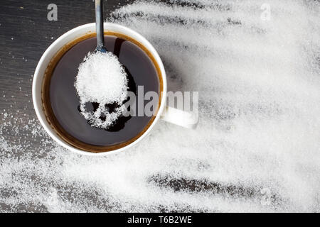 Sucre blanc malsain concept. Scull spoon avec du sucre et tasse de café noir sur fond de bois Banque D'Images