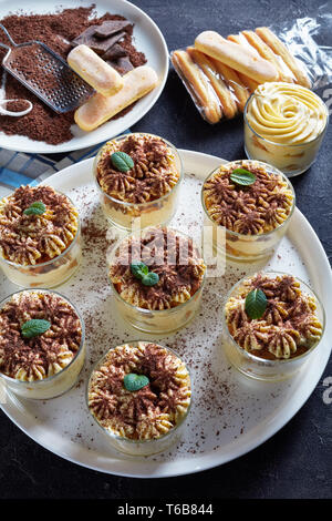 Tiramisu, dessert italien de savoiardi biscuits, oeuf, sucre, café, mascarpone à lunettes rondes sur un plateau. Ingrédients sur une table, vertical Banque D'Images