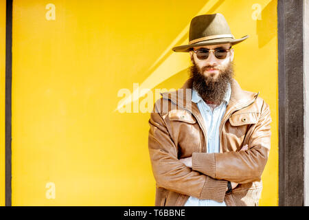 Portrait d'un homme barbu élégant habillé en veste et chapeau sur le fond jaune vif à l'extérieur Banque D'Images