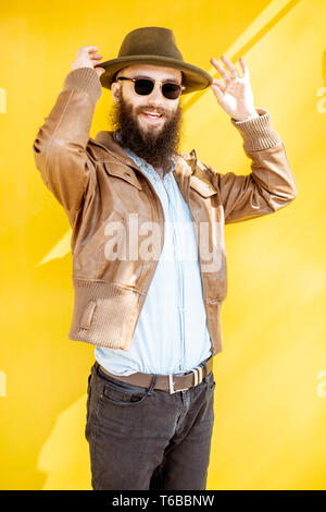 Portrait d'un homme barbu élégant habillé en veste et chapeau sur le fond jaune vif à l'extérieur Banque D'Images