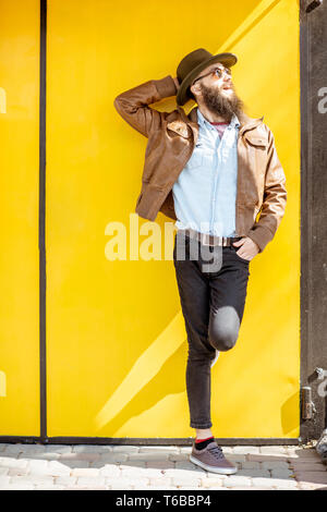 Portrait d'un homme barbu élégant habillé en veste et chapeau sur le fond jaune vif à l'extérieur Banque D'Images