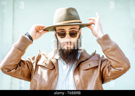 Portrait d'un homme barbu élégant wearing hat sur la lumière fond bleu turquoise à l'extérieur Banque D'Images